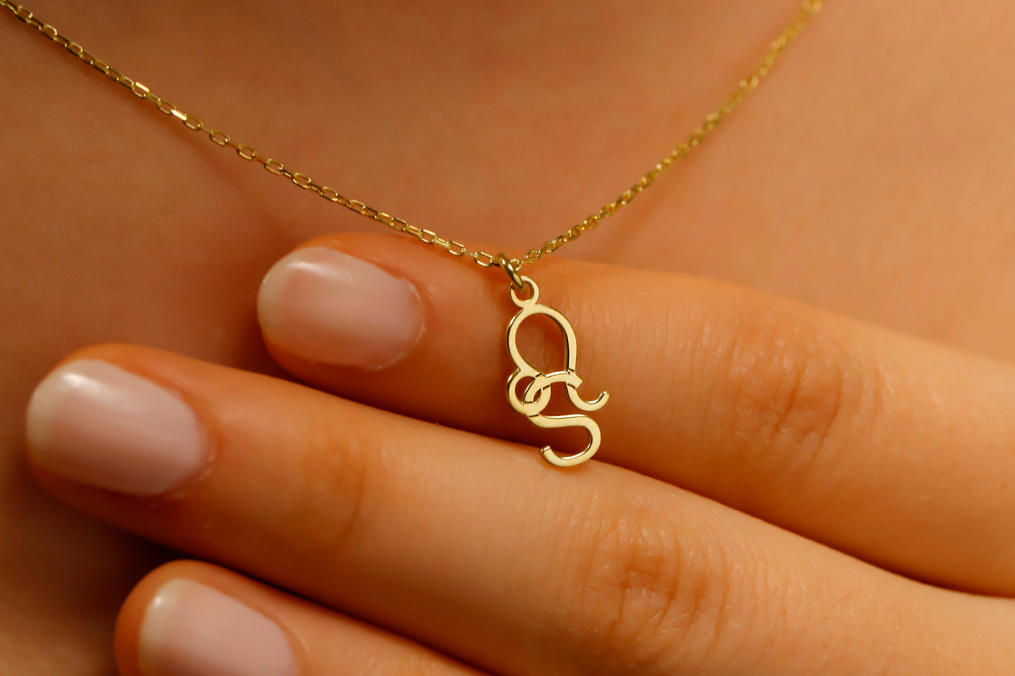 Gold necklace with a 'QS' pendant on a hand