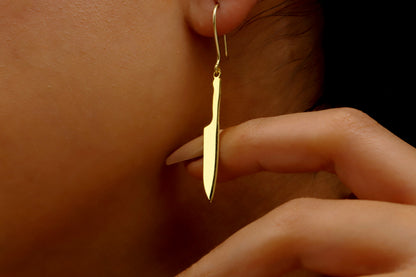 A close-up image of a person wearing a silver knife earring with a gold-filled dagger earring in their ear.