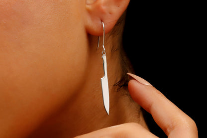 A close-up image of a person wearing a silver knife earring with a silver dagger earring in their ear.