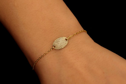 A gold-colored bracelet with a fingerprint engraving on a disc, displayed on a person's wrist.