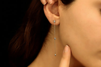 A close-up image of a woman's ear wearing a silver long chain dangle earring with a clear cubic zirconia diamond.