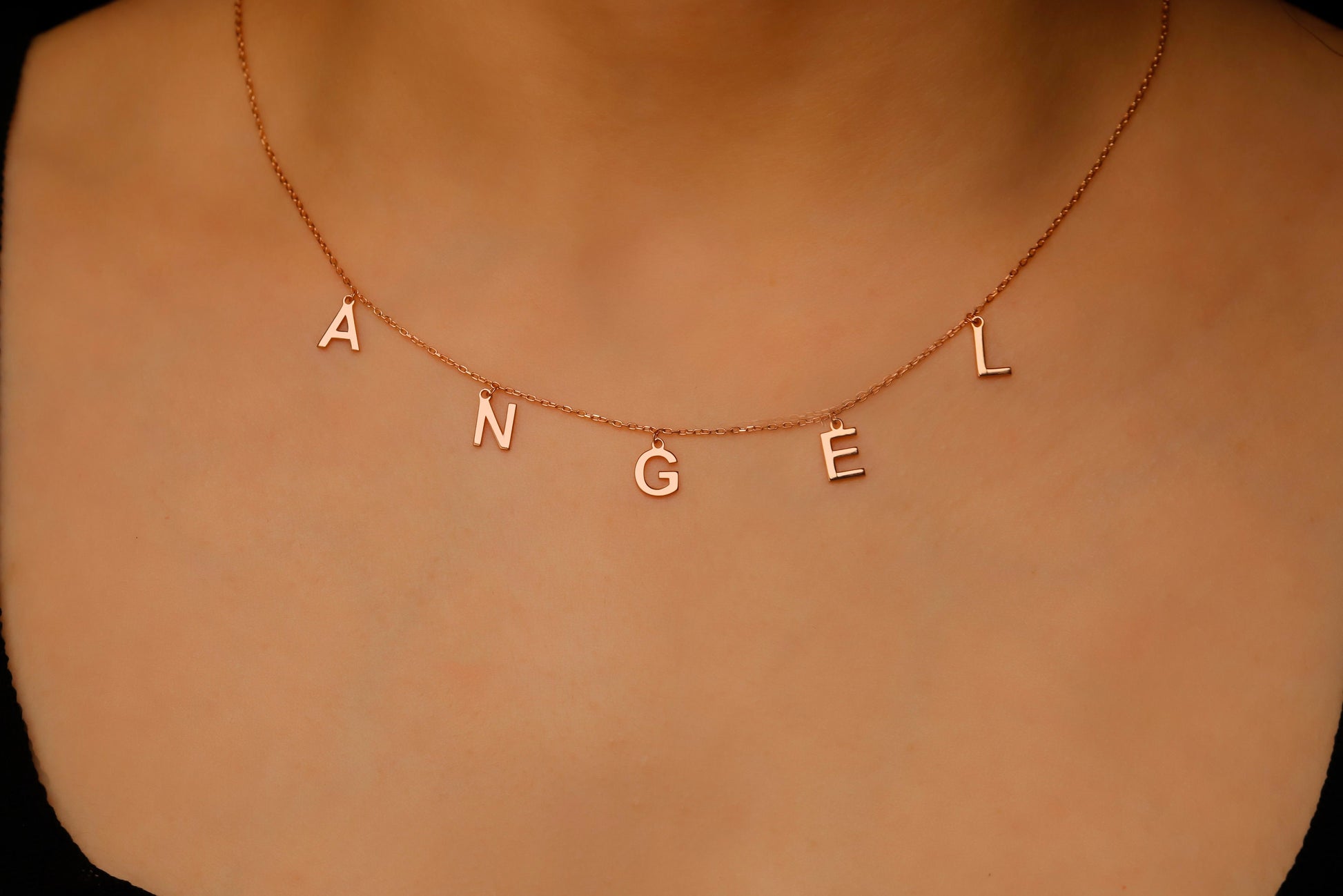 Rose gold 'ANGEL' necklace on a person's neck against a neutral background
