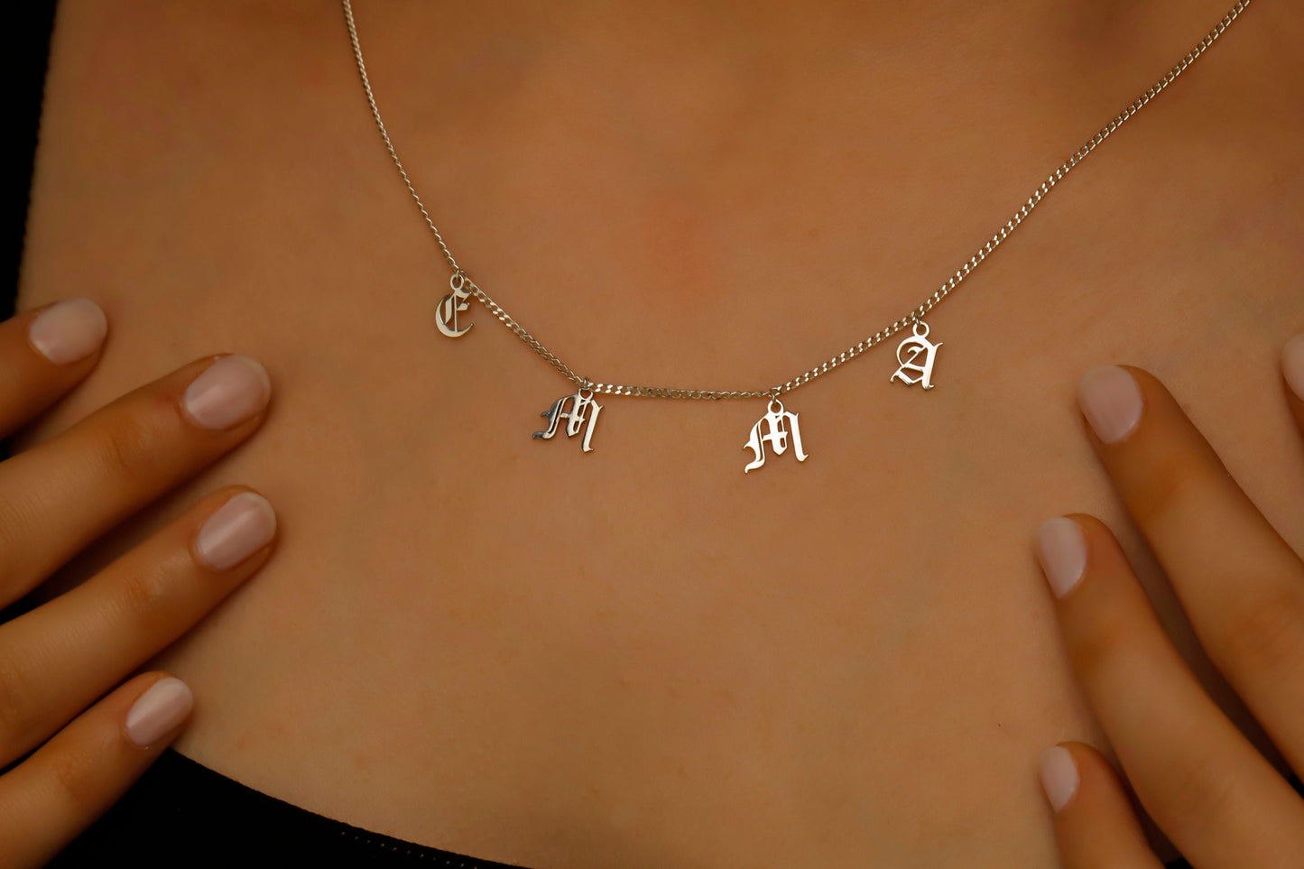 Personalized name necklace featuring dangle letters on a silver curb chain worn around the neck.