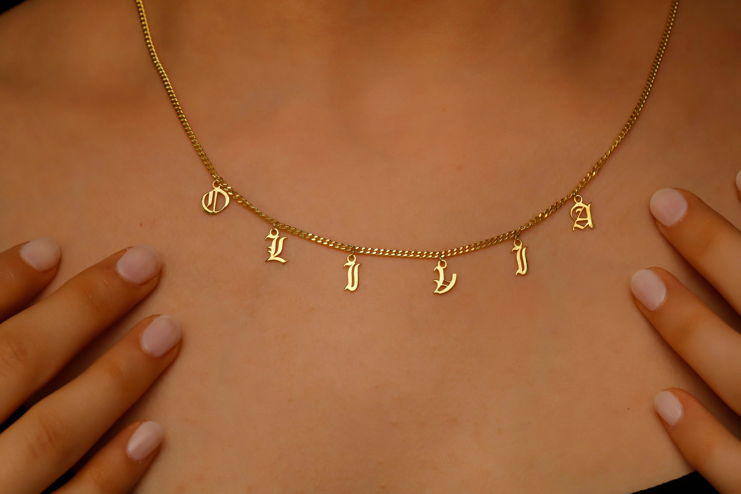 Personalized name necklace showcasing dangle Gothic Old English letters spelling 'OLIVIA' on a gold chain.