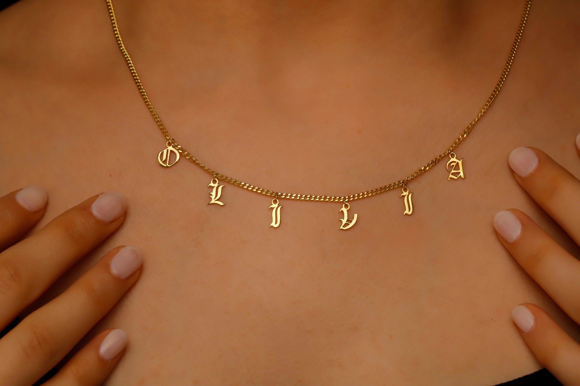 Personalized name necklace showcasing dangle Gothic Old English letters spelling 'OLIVIA' on a gold chain.
