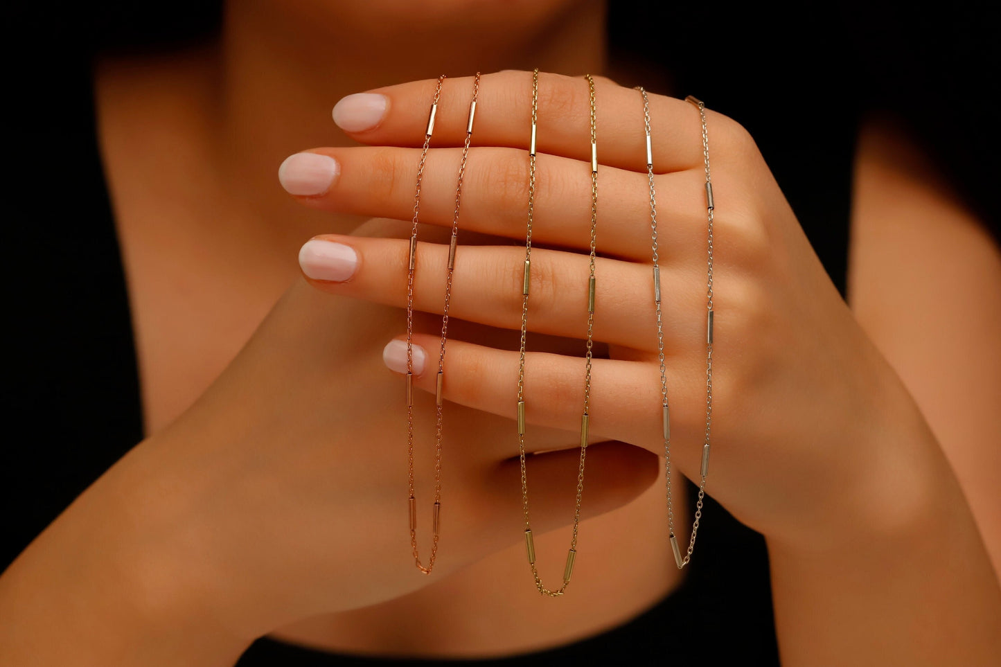 Close-up of a hand wearing multiple gold necklaces on a dark background