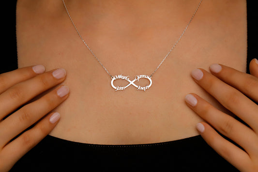 Silver infinity necklace on a person's neck with hands framing the image