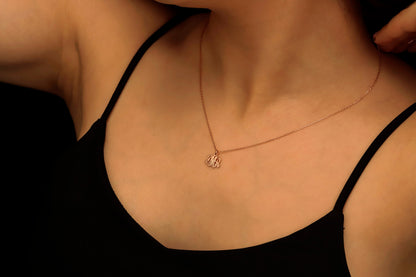 A gold monogram necklace with the initial 'S' displayed on a person's hand, highlighting the necklace's elegant cursive script design.