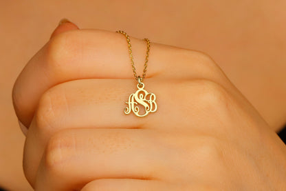 A gold monogram necklace with the initial 'S' displayed on a person's hand, highlighting the necklace's elegant cursive script design.