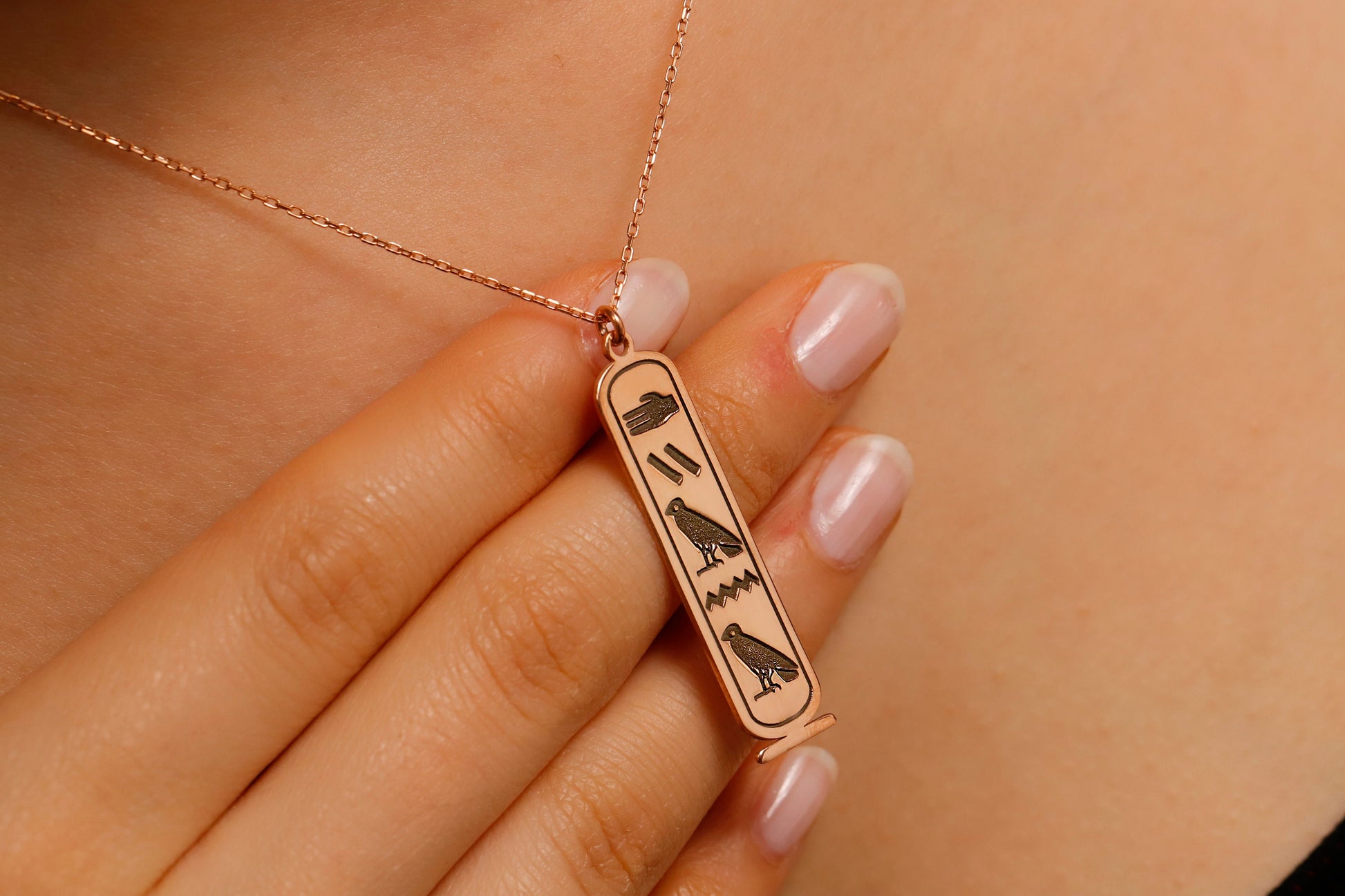 Rose gold necklace with an Egyptian hieroglyphics pendant on a blurred background
