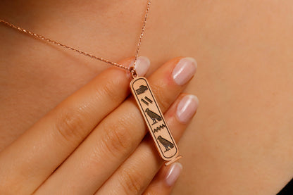 Rose gold necklace with an Egyptian hieroglyphics pendant on a blurred background