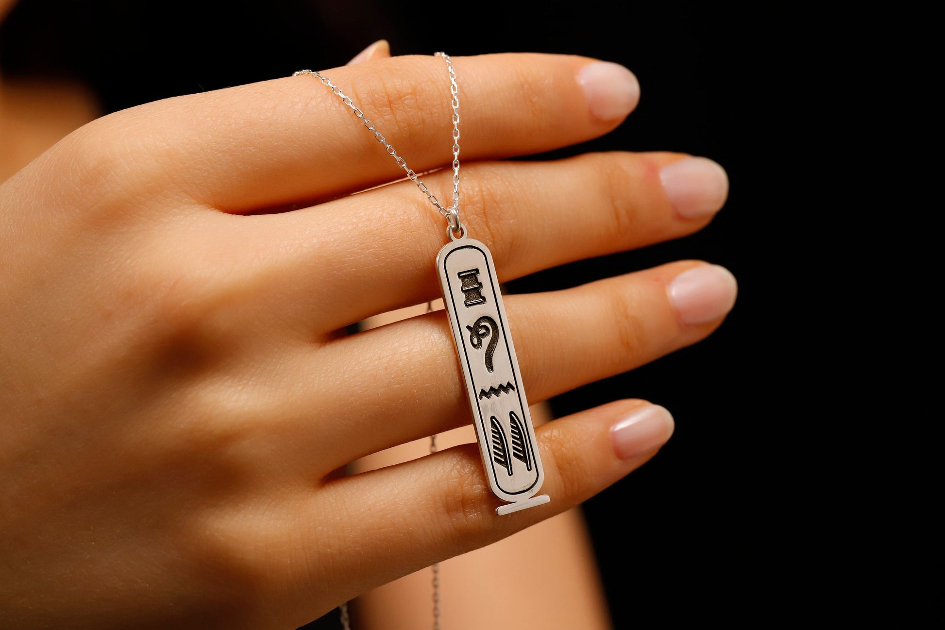 Hand holding a necklace with a pendant featuring Arabic text against a dark background