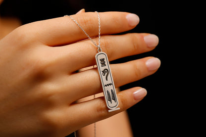 Hand holding a necklace with a pendant featuring Arabic text against a dark background