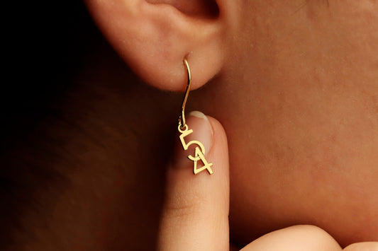 A close-up image of a woman's ear wearing a dangle earring with the number 54 in gold.