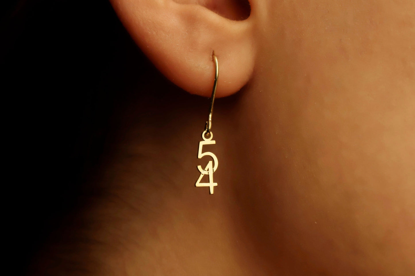 Gold hoop earring with '54' design worn on an ear.
