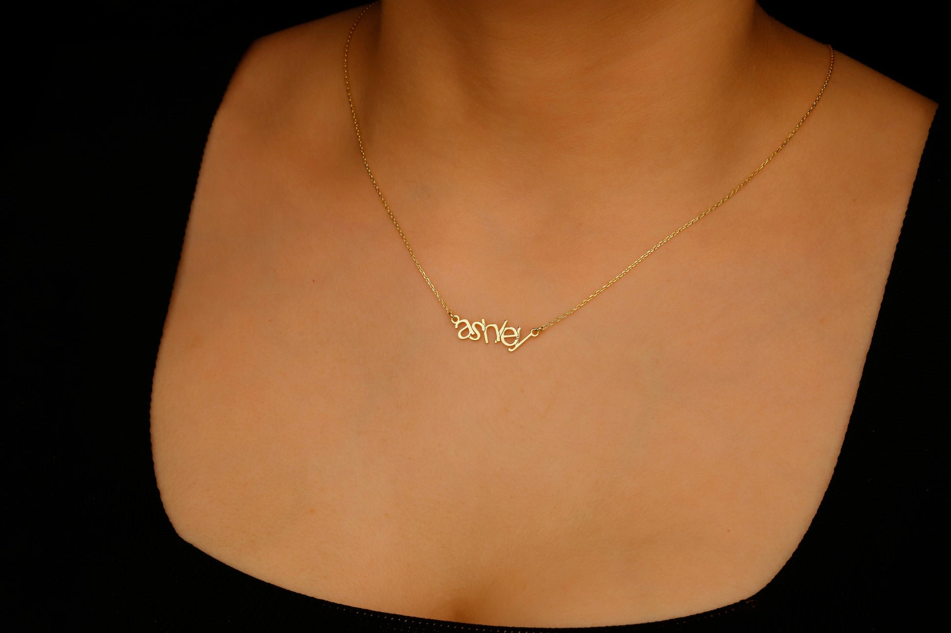 Gold necklace with 'ashe' pendant on a mannequin neck against a black background