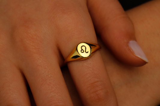 Gold ring with a zodiac symbol on a person's finger
