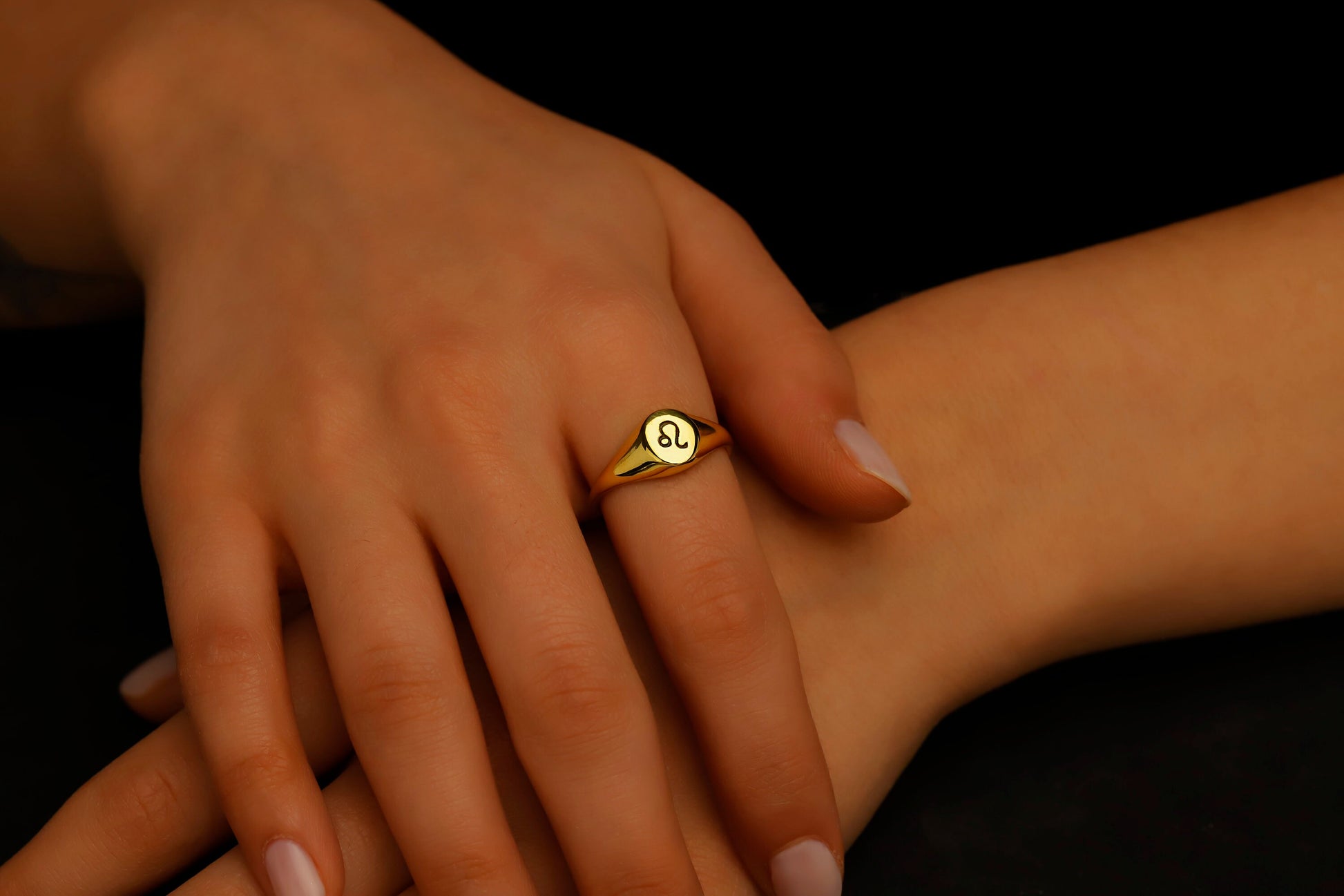 Gold ring with a symbol on a person's finger against a dark background