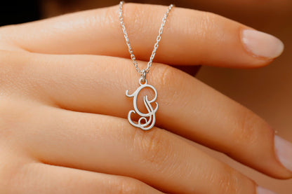 Silver necklace with a pendant held by a hand against a neutral background
