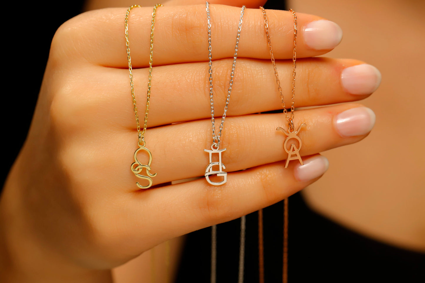 Three necklaces with different designs held by a hand against a neutral background
