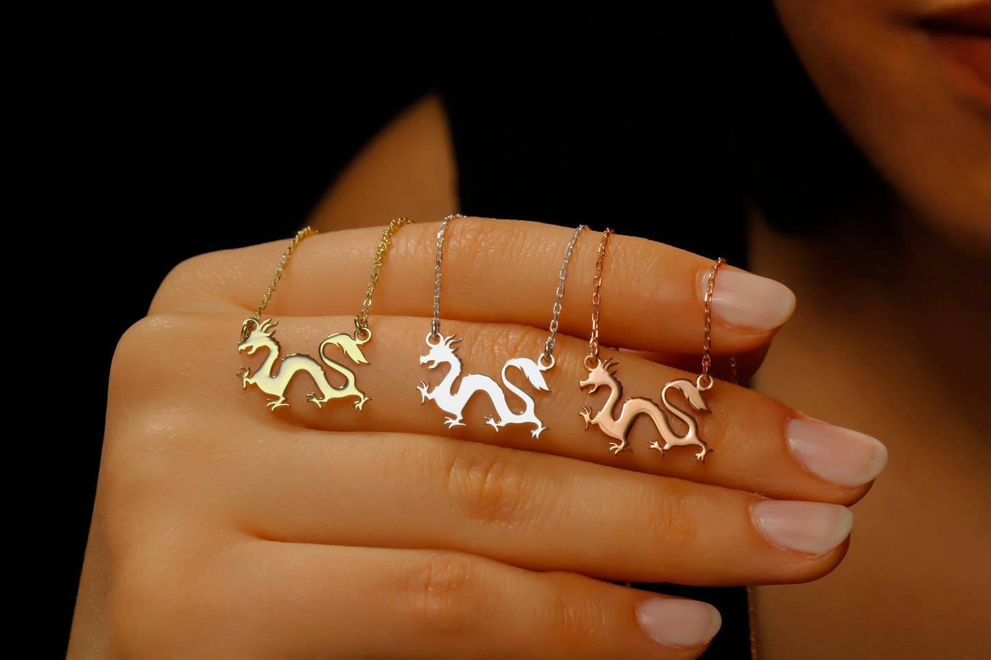 Three gold dragon necklaces on a hand against a dark background