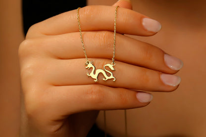 Gold necklace with a dragon pendant held in a hand against a neutral background