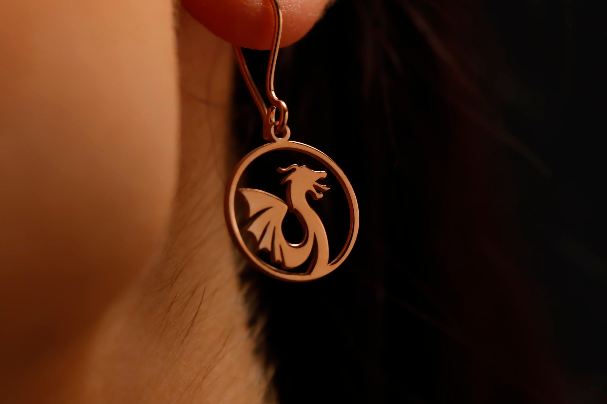 Bronze dragon-shaped earring worn on an ear with a dark background