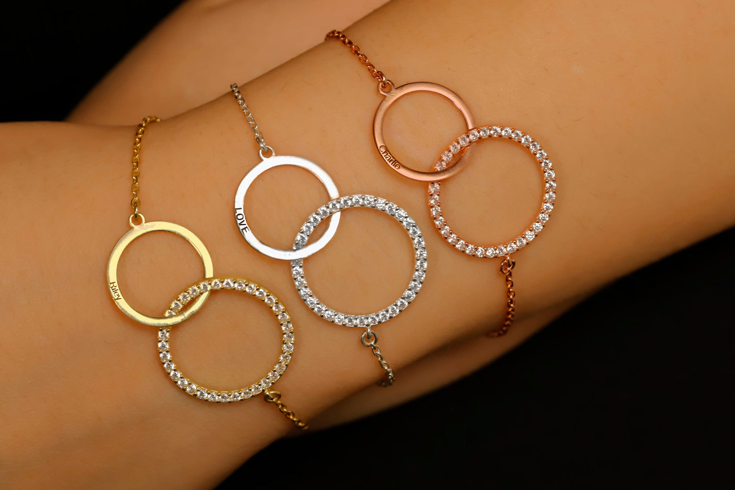 Three circular bracelets in gold, silver, and rose gold on a wrist against a dark background.