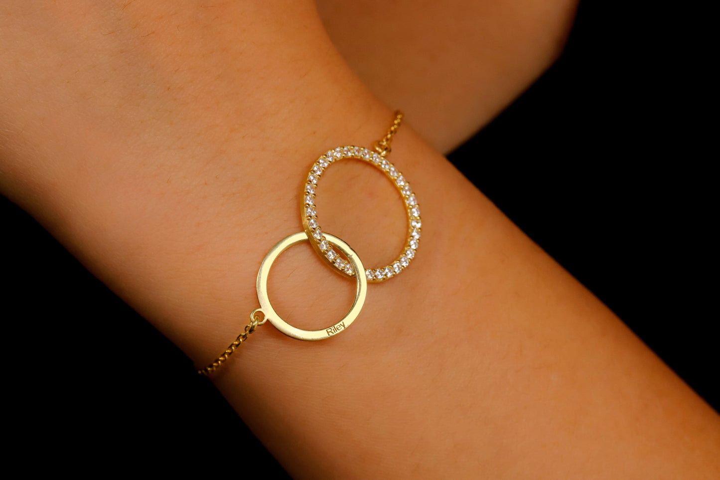 Gold bracelet with interlocking rings on a wrist against a black background