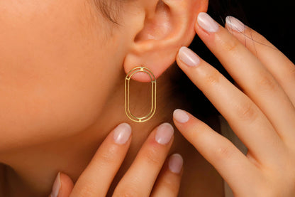 A close-up image of a woman's ear wearing a gold oval ear jacket earring.