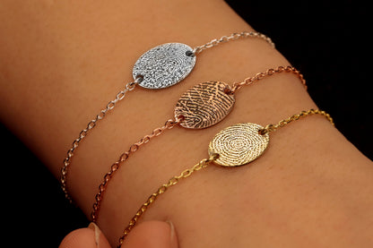 Gold rose and silver colored bracelets with a fingerprint engraving on a disc, displayed on a person's wrist.