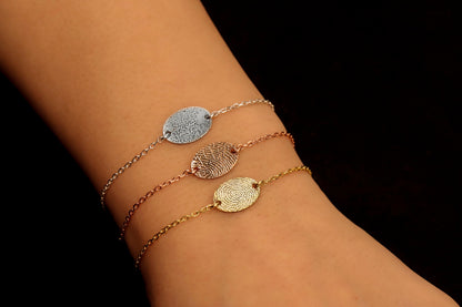 Gold rose and silver colored bracelets with a fingerprint engraving on a disc, displayed on a person's wrist.