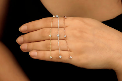 A close-up image of a woman's ear wearing a silver long chain dangle earring with a clear cubic zirconia diamond.