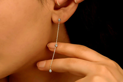 A close-up image of a woman's ear wearing a silver long chain dangle earring with a clear cubic zirconia diamond.