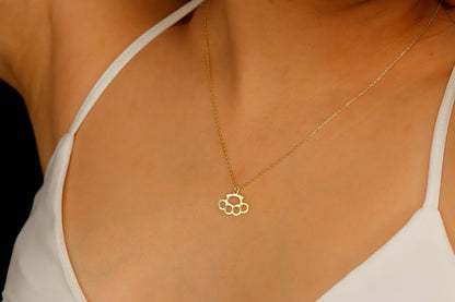A close-up image of a gold-filled necklace with a brass knuckle design being worn on a person's finger.