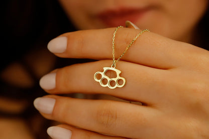 A close-up image of a gold-filled necklace with a brass knuckle design being worn on a person's finger.