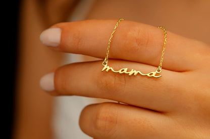 A dainty necklace with the inscription 'mama' worn by a person with a white top.