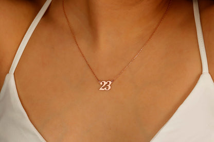 A close-up image of a woman wearing a personalized necklace with a number '23' in rose gold-tone on a silver chain.