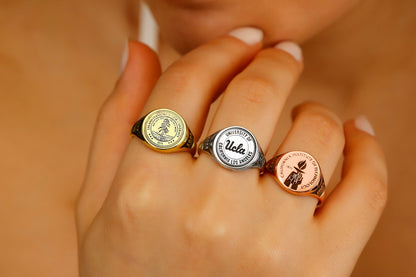 A close-up image of a person's finger wearing a college seal engraving signet ring.