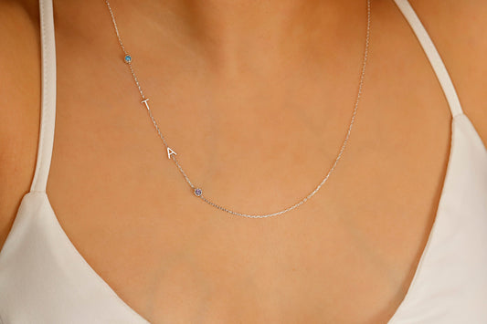 A close-up image of a sterling silver necklace with gold lettering and multicolored birthstones laid out on a person's neck.