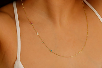 A close-up image of a sterling silver necklace with gold lettering and multicolored birthstones laid out on a person's neck.