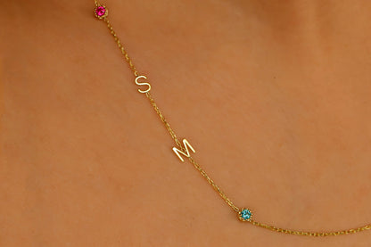 A close-up image of a sterling silver necklace with gold lettering and multicolored birthstones laid out on a person's neck.