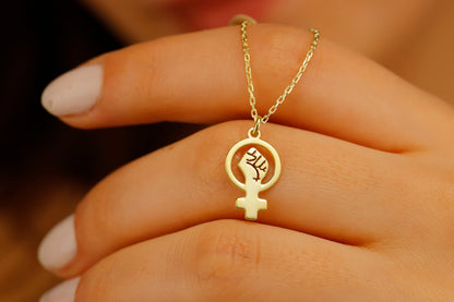 A gold necklace with a Venus symbol pendant, resting on a person's hand.