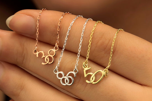 Three personalized interlock lucky numbers necklaces in silver, gold, and rose colors, displayed on a hand.