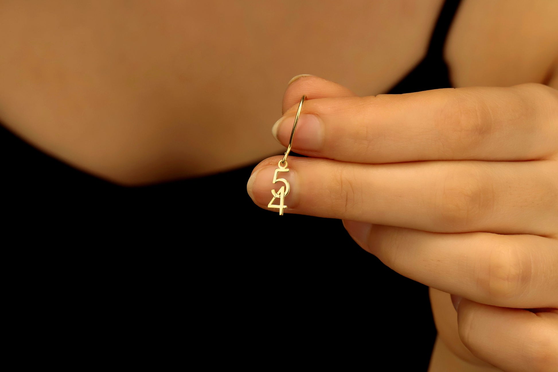 Gold earring with a design held between fingers against a dark background
