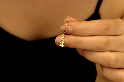 Gold earring with a design held between fingers against a dark background