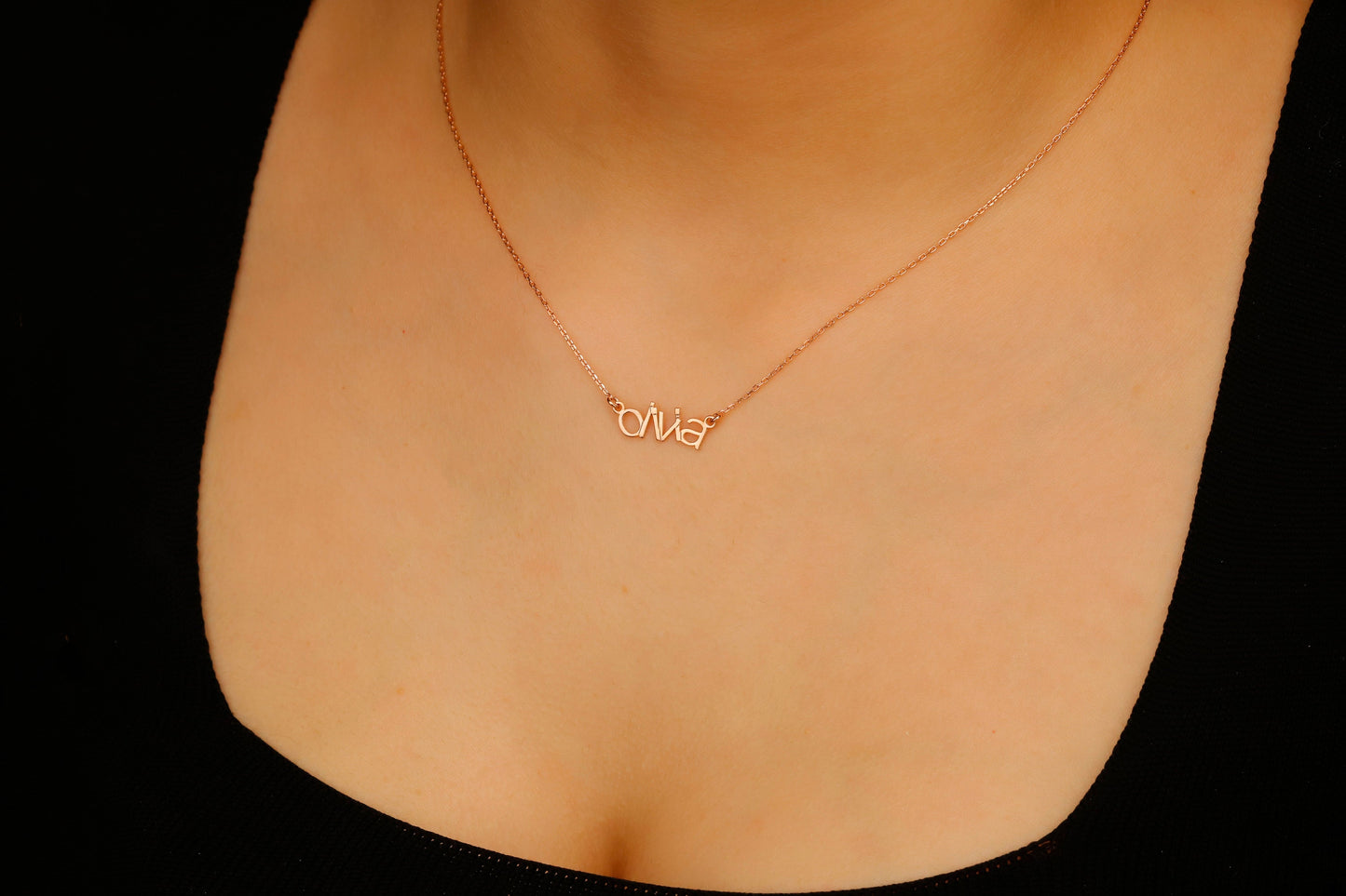 Rose gold necklace with a name pendant on a person's neck against a black background