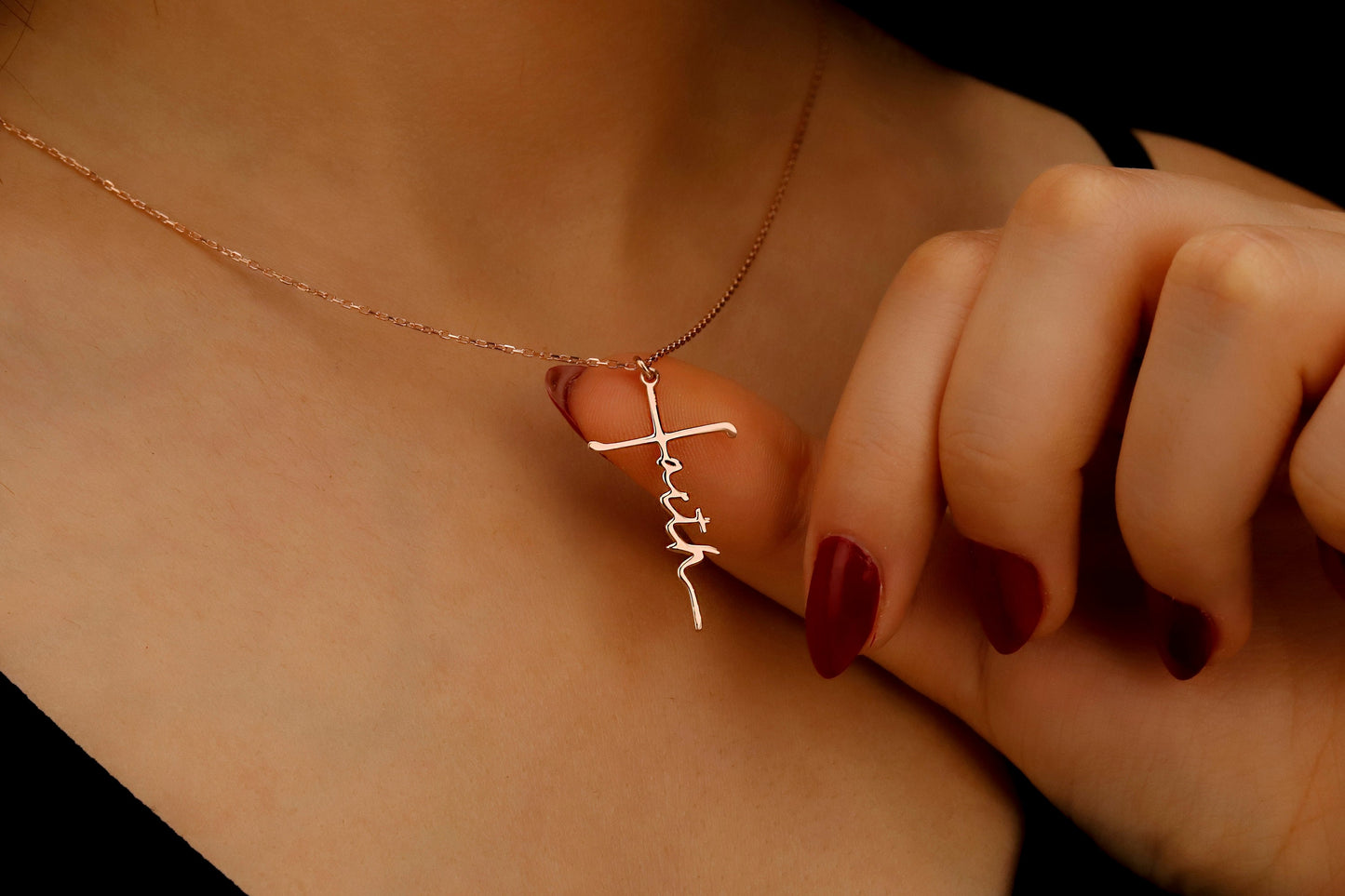 Necklace with a cross pendant worn by a person with red nail polish.
