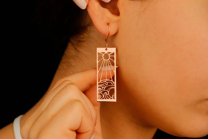 A person wearing a dangle earrings with a sun and ocean wave design.