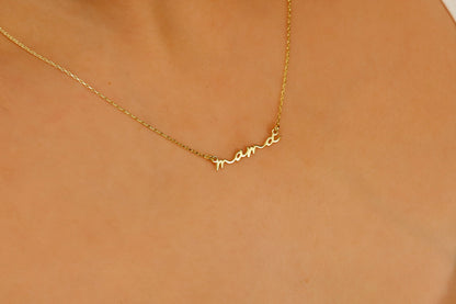 A dainty necklace with the inscription 'mama' worn by a person with a white top.